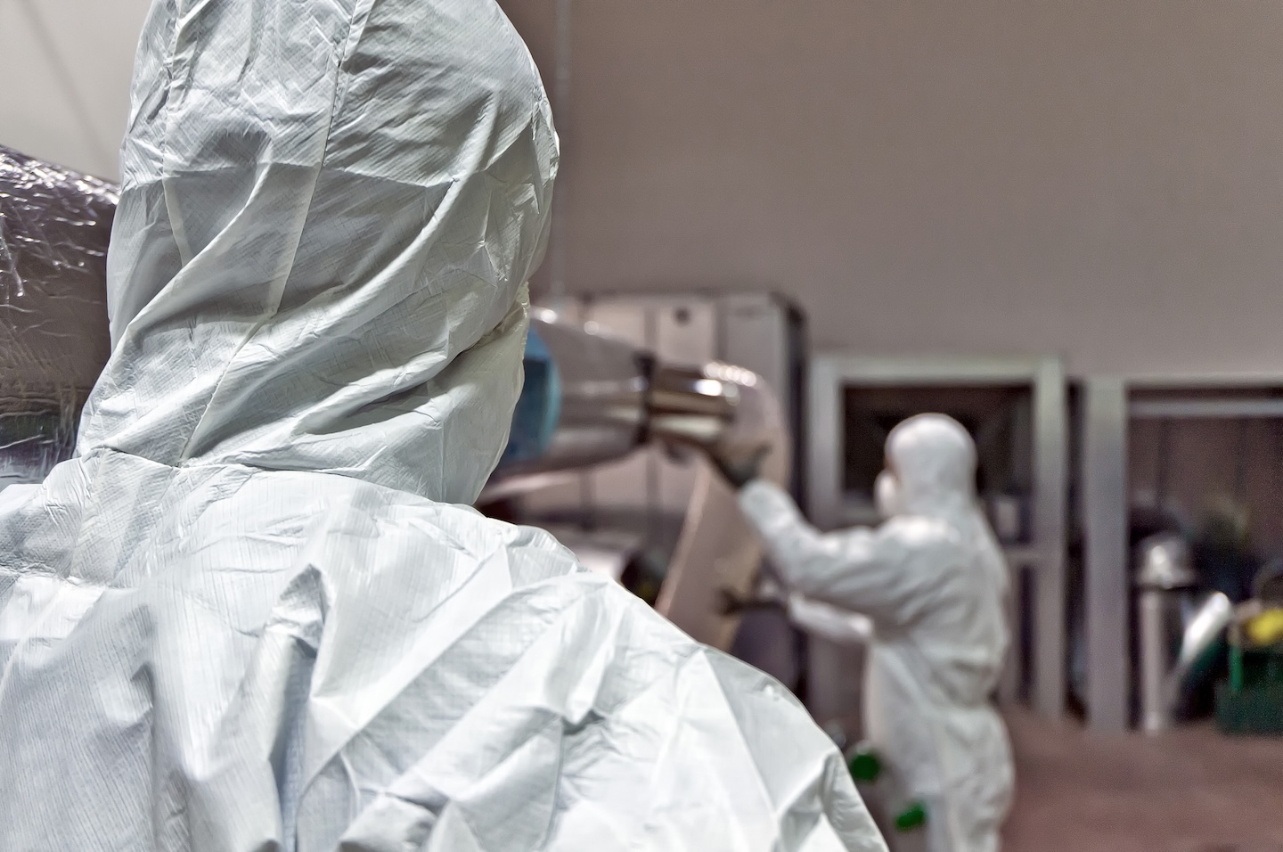 Immagine di due operatori vestiti con dispositivi di protezione avanzati, intenti nella rimozione di materiali pericolosi, Servizio di rimozione amianto di L'Orologio Societ&agrave; Cooperativa.